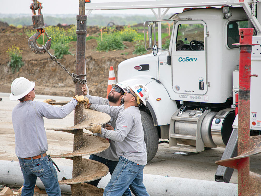 CoServ linemen install the drilling bit on the boom tip.